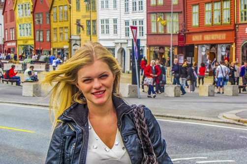 Bilde illustrerer en kvinnelig student i Bergen, fotografert foran karakteristiske bryggen