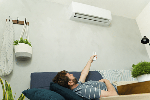 Bilde viser en mann liggende på sofa som styrer varmepumpe på vegg med fjernkontroll