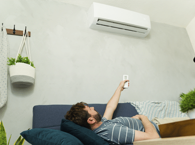Bilde viser en mann liggende på sofa som styrer varmepumpe på vegg med fjernkontroll