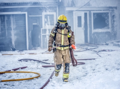 Bilde viser en brannmann gående vekk fra brannskadet hus vinterstid