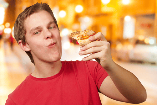 Bilde viser en ung gutt som spiser varm pizza i byen