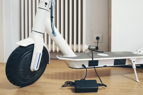 Bilde viser en hvit elsparkesykkel som står til lading innendørs